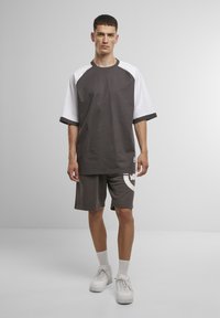 Gray and white color-blocked oversized t-shirt with raglan sleeves, paired with gray athletic shorts featuring a white logo accent and plain white sneakers.