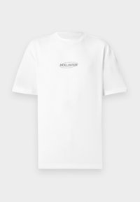 Λευκό T-shirt με κοντό μανίκι και μικρό γκρι λογότυπο «Hollister» στο κέντρο του στήθους, σε απλό φόντο.