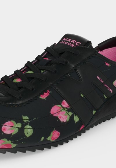 Baskets noires avec imprimé de roses roses, lacets noirs et marquage Marc Jacobs rose sur la languette et le côté, doublure intérieure rose visible.