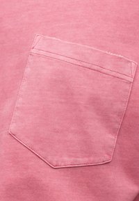 Ροζ βαμβακερό ύφασμα με ραμμένη τσέπη. Μαλακή υφή, ελαφρώς ξεθωριασμένη εμφάνιση, με διπλή ραφή κατά μήκος της άκρης της τσέπης.