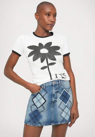 Hvid t-shirt med sort blomster grafik, suppleret af en denim nederdel med diamantmønstre i varierende blå nuancer og sort syning.