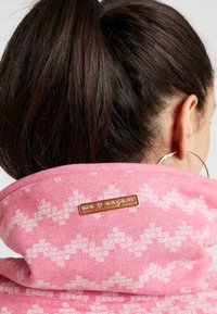 Felpa rosa con un motivo ricamato bianco e una patch in pelle "we ❤️ vegan" sul colletto, realizzata in un tessuto morbido e testurizzato.