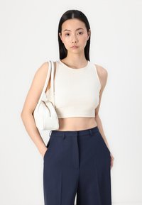 Top cropped canelado creme com decote redondo, combinado com calças de cintura alta azul-marinho e uma pequena mala branca com fecho de zíper.