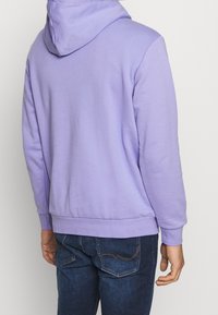 Lavendelfärgad hoodie med kenguruficka, ribs i ärmsluten och nederkant. Tyget ser mjukt och borstat ut, med en figurnära silhuett.