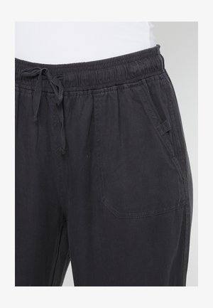 Pantaloni negri, cu talie elastică și șnur, cu buzunare laterale și o croială lejeră. Făcuți dintr-un material ușor, moale, cu o textură netedă.