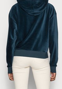 Mörkblå kordflöjts-hoodie med fodrad insida, känguruficka och ribbad fåll. Kombinerad med ljusbeige figurnära byxor.