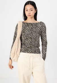 Bluză cu imprimeu leopard cu mânecă lungă în nuanțe de bej și negru, asortată cu pantaloni crem cu talie elastică și o geantă de umăr pufoasă de culoare bej.