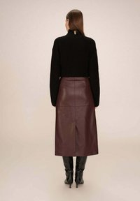 Pull noir en tricot avec un col haut, associé à une jupe midi en cuir bordeaux avec une fente dans le dos, et des bottes à talons noires.