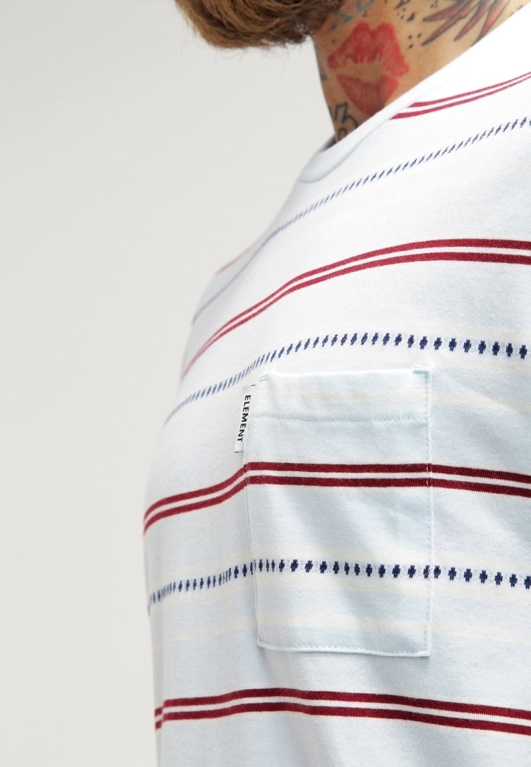Gros plan sur une personne portant une chemise blanche avec des rayures horizontales rouges et bleues, une poche avant portant l'inscription "ELEMENT" et des tatouages visibles sur le cou.