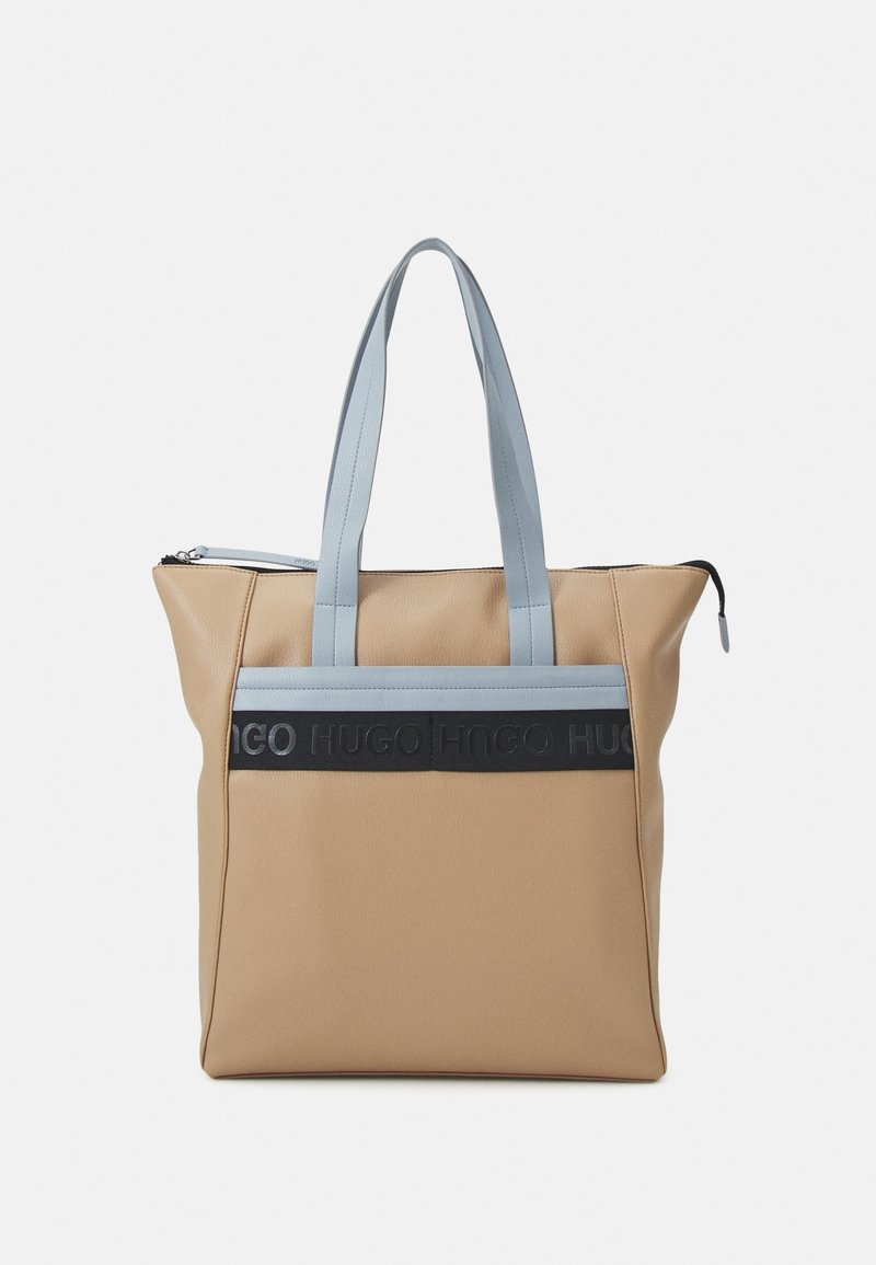 Sac fourre-tout beige avec poignées bleu clair, bande horizontale noire avec nom de la marque en relief, et fermeture éclair au sommet.