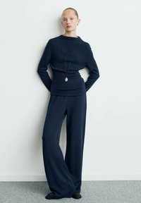 Maglione blu navy lavorato a maglia con collo alto e maniche lunghe, abbinato a pantaloni larghi blu navy. Design minimalista con una texture liscia.