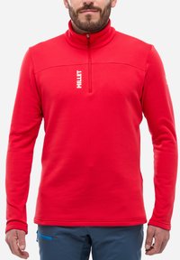 Pull en polaire rouge avec un col montant et une fermeture éclair moitié, présentant un logo blanc sur la poitrine et des coutures plates pour une texture lisse.