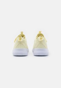 Para jasnobeżowych, dzianinowych sneakersów z białymi, teksturowanymi podeszwami, widocznych z tyłu na białym tle.