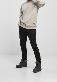 Beige sweatshirt with crew neck and logo, paired with black slim-fit pants and grey ankle boots featuring laces and durable sole.