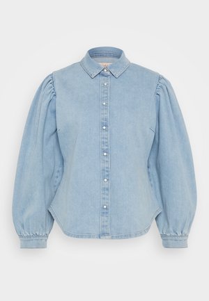 Világoskék farmering, hegyes gallérral, gombos elejével és puffos ujjakkal. Görbült hem és sima textúra jellemzi.