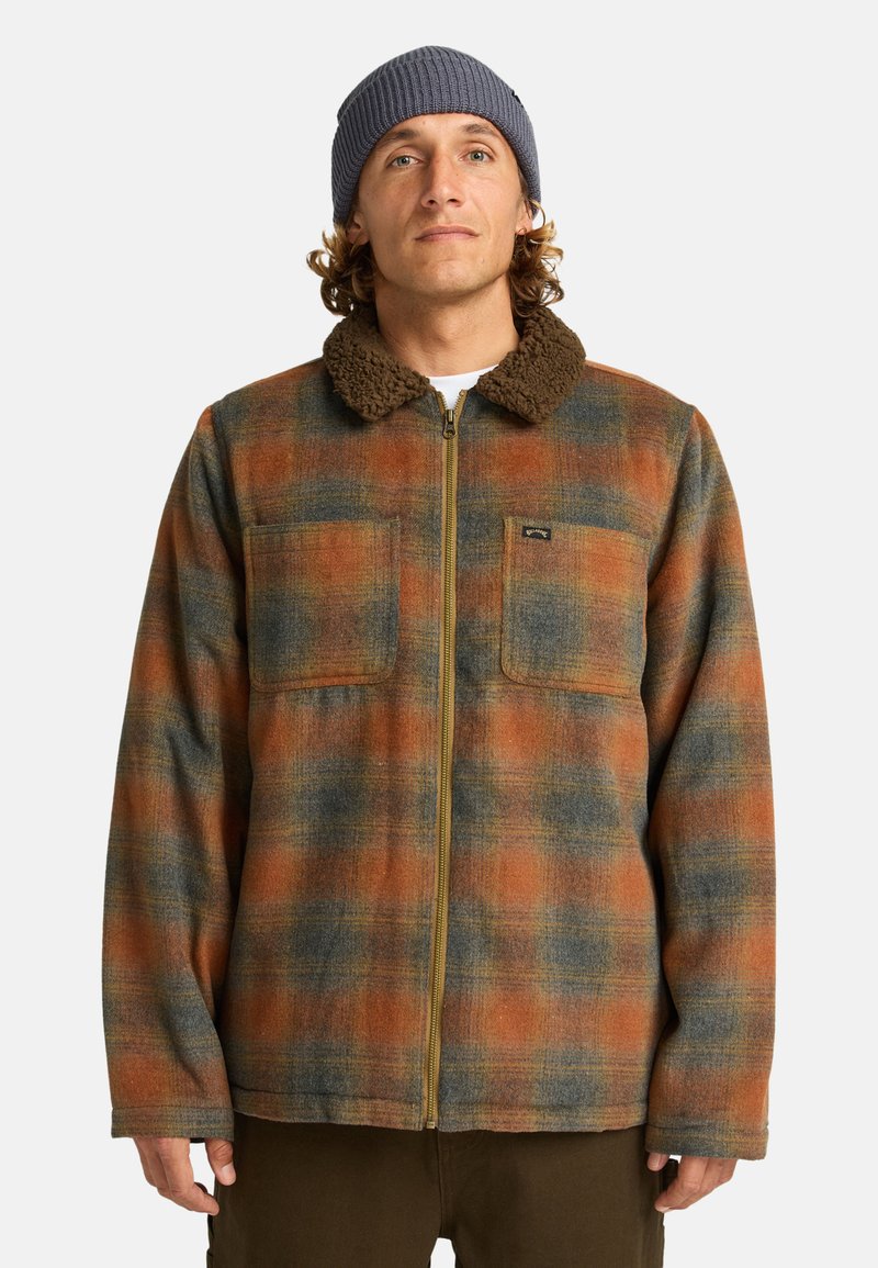 Ruitjes flanellen jas in oranje, blauw en groene tinten met een bruine sherpa kraag en twee borstzakken. Volledig met rits te sluiten.