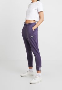 Lila joggerbyxor med justerbar dragsko i midjan och sidofickor. Har vita rands detaljer vid mudden och en broderad logotyp.