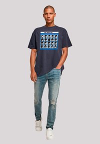 Navy cotton graphic t-shirt featuring a collage of faces in white and black with blue accents, paired with light distressed denim and white sneakers.