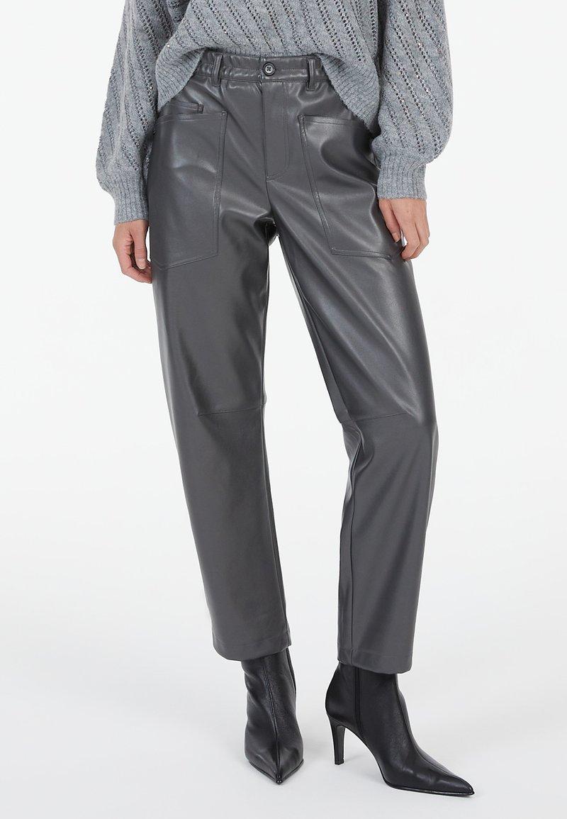 Graue Kunstlederhose mit lockerer Passform, ausgestattet mit Fronttaschen und einem Knopfverschluss, kombiniert mit eleganten schwarzen Ankle Boots mit spitzer Zehenform.