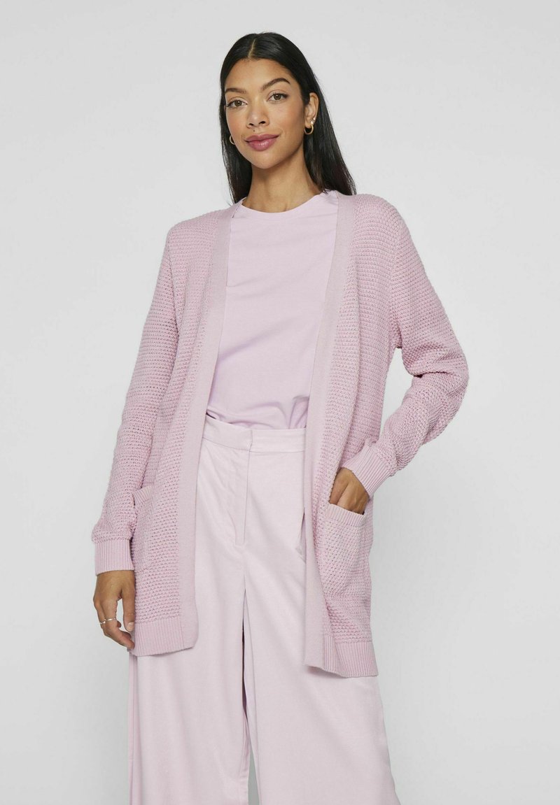 Cardigan lavorato a maglia rosa chiaro con polsini e orlo a coste, caratterizzato da un'apertura frontale e due tasche anteriori, abbinato a un top coordinato.