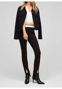 Svart kort jacka med två framfickor, vit V-ringad topp, bruna åtsittande byxor med sidokilar och svarta spetsiga ankelstövlar.