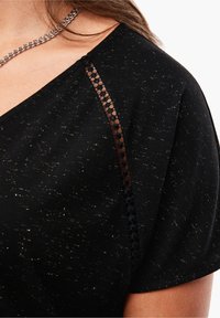 Haut noir avec des paillettes dorées, présentant un col en V et de délicates accents en dentelle noire sur les épaules. Tissu doux et texturé.