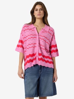 Femme portant un cardigan tricoté à manches courtes rayé rose et rouge avec des boutons, assorti à un short en jean ample arrivant aux genoux.