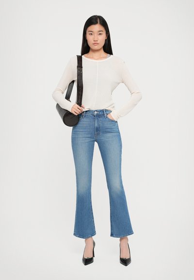 Crème top met lange mouwen, lichtblauwe high-waisted flared jeans en zwarte gepatineerde hakken. Ronde zwarte handtas met een schouderband.