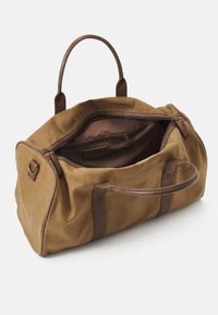 Sac de sport en toile marron avec des poignées et des accents en cuir marron foncé. Dispose d'un intérieur spacieux et ouvert avec une poche zippée.