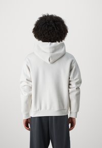 Bílá mikina s kapucí a měkkou texturou, s klokaní kapsou a žebrovanými manžetami. Nosit s tmavě šedými kalhotami.