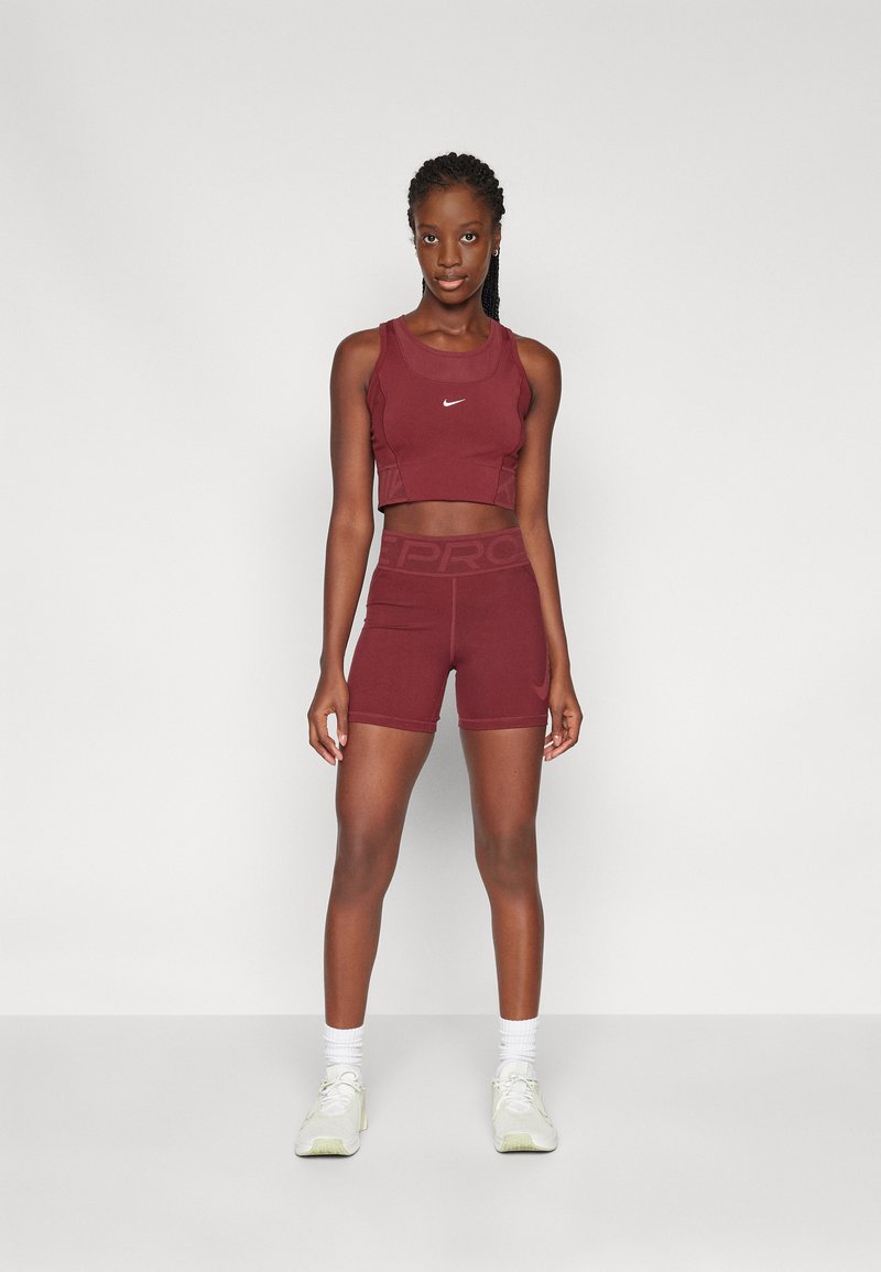Top deportivo corto burdeos con diseño de espalda cruzada, combinado con pantalones cortos ajustados a juego. Presenta el logotipo de Nike en blanco en ambas prendas. Tela texturizada.