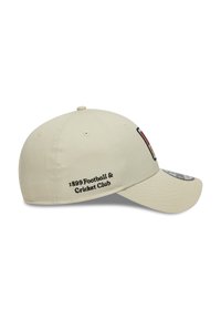 Beige baseball cap with curved brim, embroidered "1899 Football & Cricket Club" text, and a logo badge on the front. Smooth fabric texture.