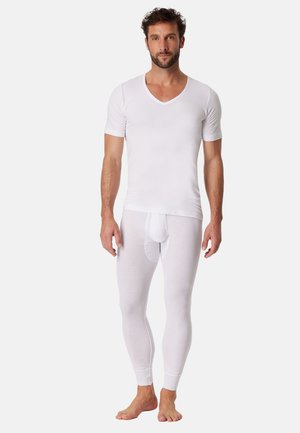 Man wearing white short-sleeve V-neck shirt and matching white long underwear bottoms, standing barefoot against a plain background.