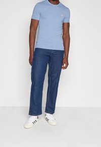 Lyseblå kortærmet t-shirt med et lille rosa trekantet logo, parret med mørkeblå lige bukser og hvide sneakers med sorte striber.