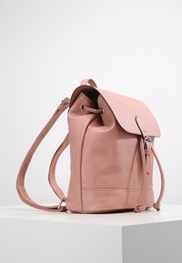 Zaino in finta pelle rosa con chiusura a coulisse, superficie liscia, parte superiore arrotondata e spallacci regolabili.