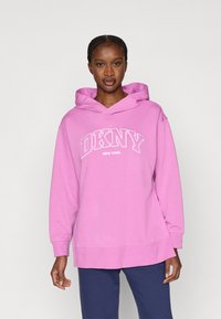 Roosa DKNY dressipluus nööriga kapuutsi, valge logoga ja tekstiga, pikkade varrukatega ning lõdva istuvusega. Kangas tundub pehme ja ühtlase tekstuuriga.