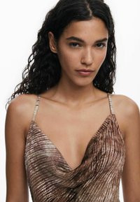 Barna, ujjatlan ruha texturált, hullámszerű mintázattal. Mély V-kivágással és vékony pántokkal rendelkezik. Puha anyag, amely folyékony esést biztosít.