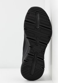 Suela de zapato deportivo negro con una superficie texturizada y con patrones que presenta surcos para agarre y una sección central lisa.