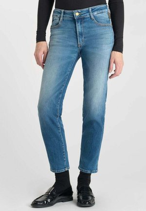Hellblaue Jeans im Slim-Fit-Schnitt mit fünf Taschen, Knopfverschluss und dezentem Verblassen. Kombiniert mit schwarzen Mokassins und Socken.