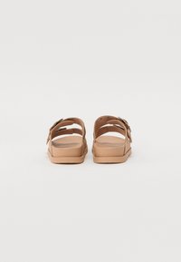 Infradito marroni con due cinturini regolabili, caratterizzati da una superficie liscia e una leggera texture, suola piatta e fibbie sottili.