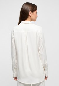 Witte langslippige shirt met een kraag, gladde stof, plooi aan de achterkant en met knopen sluitende manchetten, met een klassieke, relaxte pasvorm.