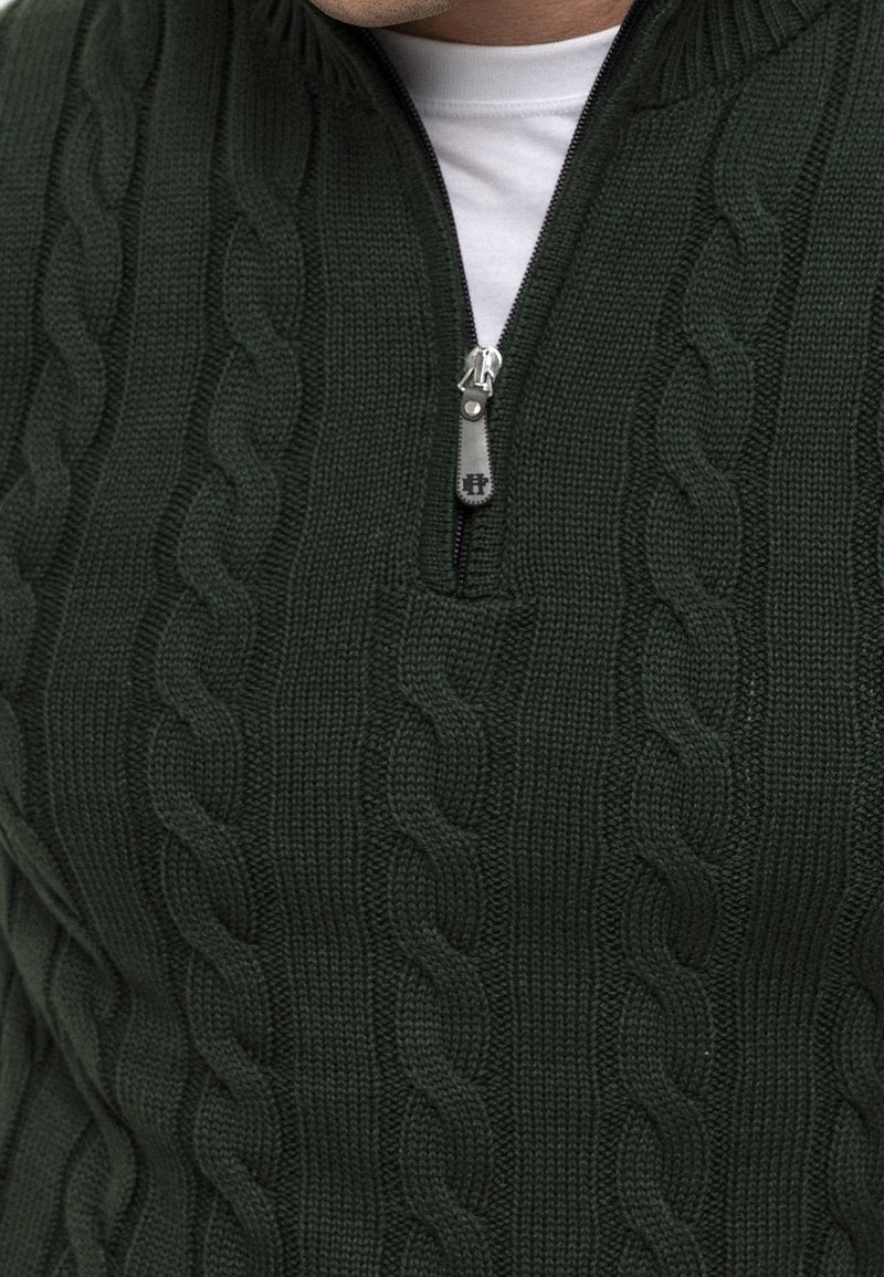 Ciemnozielony dziergany sweter z kołnierzem na półzamek, z wzorem warkoczowym i teksturowanym wykończeniem. Srebrny suwak.