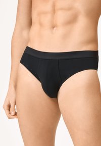 Culotte en coton noir avec une taille élastique, présentant une texture lisse et une coupe ajustée. Aucun motif ni détail matériel visible.