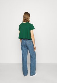 T-shirt vert, coupe courte avec des manches courtes, présentant une coupe décontractée. Associé à un jean bleu taille haute à jambe large, porté avec des chaussures blanches.