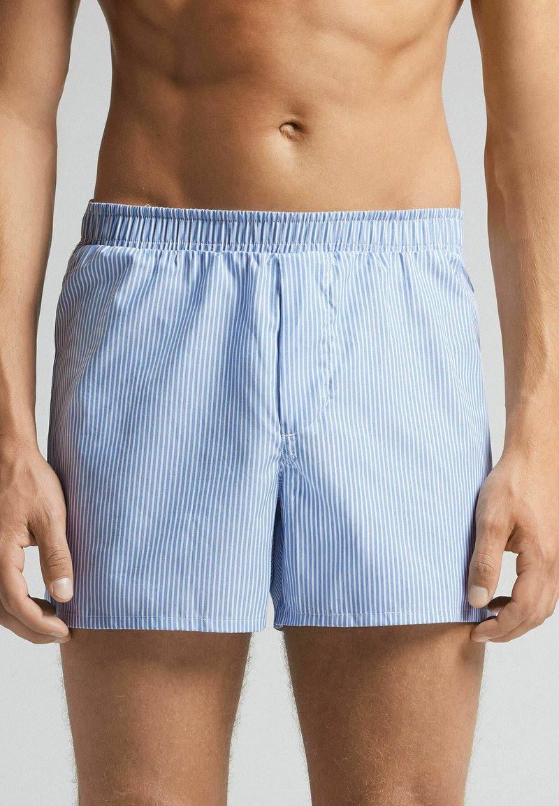 Blue and white striped swim shorts with an elastic waistband, soft fabric, and a relaxed fit. Features a front seam and no pockets.
