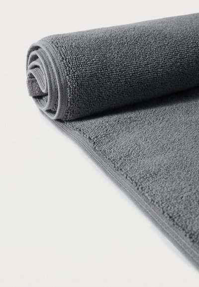 Συσπειρωμένη σκούρα γκρι υφασμάτινη πετσέτα μπάνιου σε λευκή επιφάνεια με εμφανές μοτίβο ύφανσης και ραμμένα άκρα.