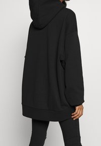 Sudadera negra de gran tamaño hecha de tejido suave, con capucha, mangas largas y dobladillo acanalado. Sin patrones visibles ni herrajes.