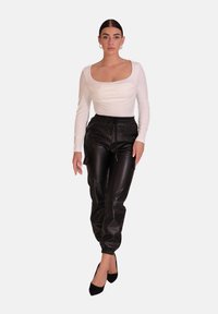 Witte top met lange mouwen en een vierkante halslijn, gecombineerd met zwarte joggingbroeken van imitatieleer met een elastische tailleband en nauwsluitende boorden. Zwarte hakken.