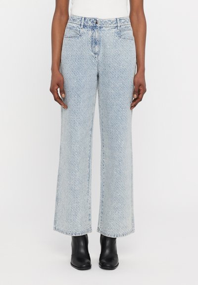 Jeans de denim de culoare albastru deschis, cu picioare largi, prezentând fadii subtile și un croi drept, asortați cu cizme negre până la gleznă.