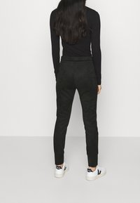 Svarta mockajoggers med en tapered passform och elastisk midja. Kombinationen med vita sneakers med svarta accenter.